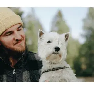 Hombre cargando a un perro blanco. Foto: Pexels/PNW Production
